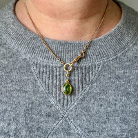 Necklace with a green pendant worn by a person in a gray sweater.