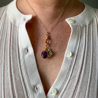 Necklace with a purple gemstone pendant worn by a person in a white shirt.
