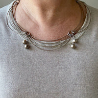 Silver necklace with beads worn by a person on a plain background