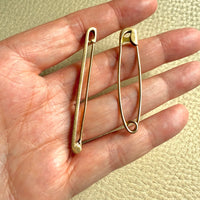 Two gold safety pins held between fingers against a beige background