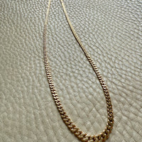 Gold chain necklace on a textured beige surface