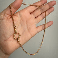 Gold chain held in a hand against a plain background