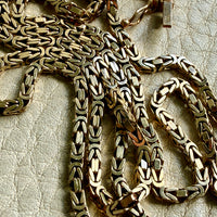 14k gold Gold byzantine chain necklace on a textured beige surface penelopepenelope.com fine jewelry