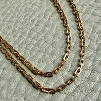 Two gold chain necklaces on a textured light gray background