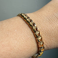 Gold chain bracelet on a wrist against a neutral background