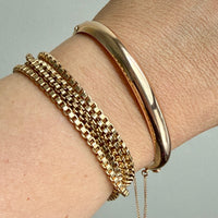 Gold bracelets on a wrist against a neutral background