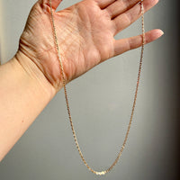 Gold chain held by a hand against a neutral background