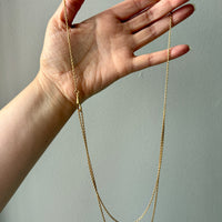 Gold chain necklace held by a hand against a plain background