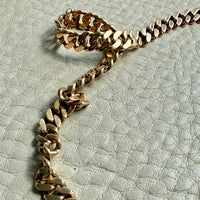 Gold chain on a textured light gray background. PenelopePenelope.com