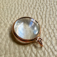 Clear glass antique pendant locket with gold setting on a textured beige surface