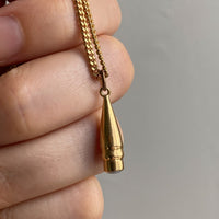An 18k gold vintage-style charm featuring a pearl set in the tip, held in a person's hand.
