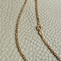 Gold chain necklace on a textured beige surface