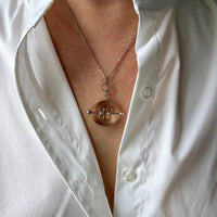 A person wearing a white shirt displaying a vintage silver and quartz pendant necklace by Elis Kauppi with a central oval pendant, arced silver wedges, and clear quartz crystals.