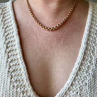 Necklace worn by a person wearing a beige knitted cardigan.