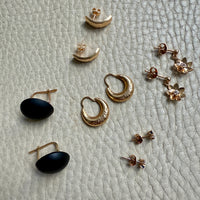 Collection of gold and rose gold earrings on a textured light gray surface