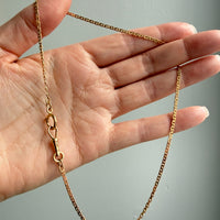 Gold chain held by a hand against a gray background
