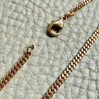 18k Gold curb chain necklace on a textured light surface