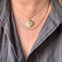 Close-up of a person wearing a gold necklace with a pendant.