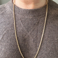 Gold chain necklace on a person wearing a gray sweater.