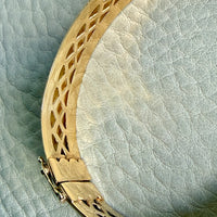 Gold bracelet with intricate design on a textured light blue background