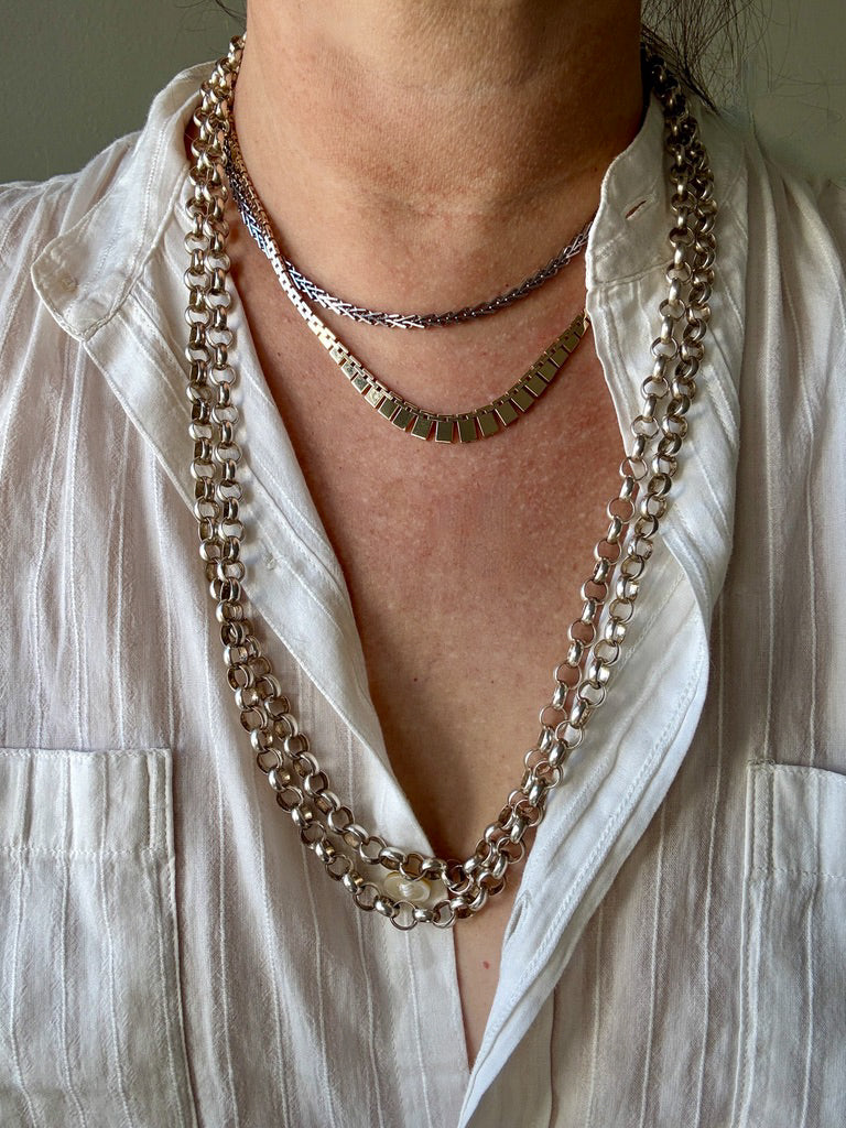 Close-up of a person wearing multiple necklaces with a white shirt.