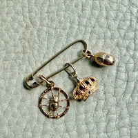 Gold brooch with a wheel and crown charm on a textured light green background