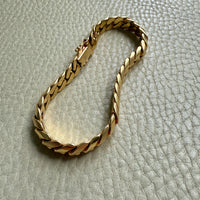 Gold chain bracelet on a textured light gray surface