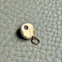 Small round gold charm with an orange stone on a textured light gray surface
