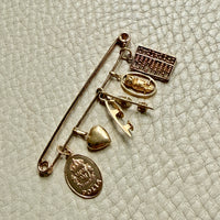 Gold brooch with various charms on a textured light background. PenelopePenelope.com