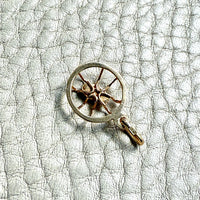 Gold pendant with spider design on a textured white surface