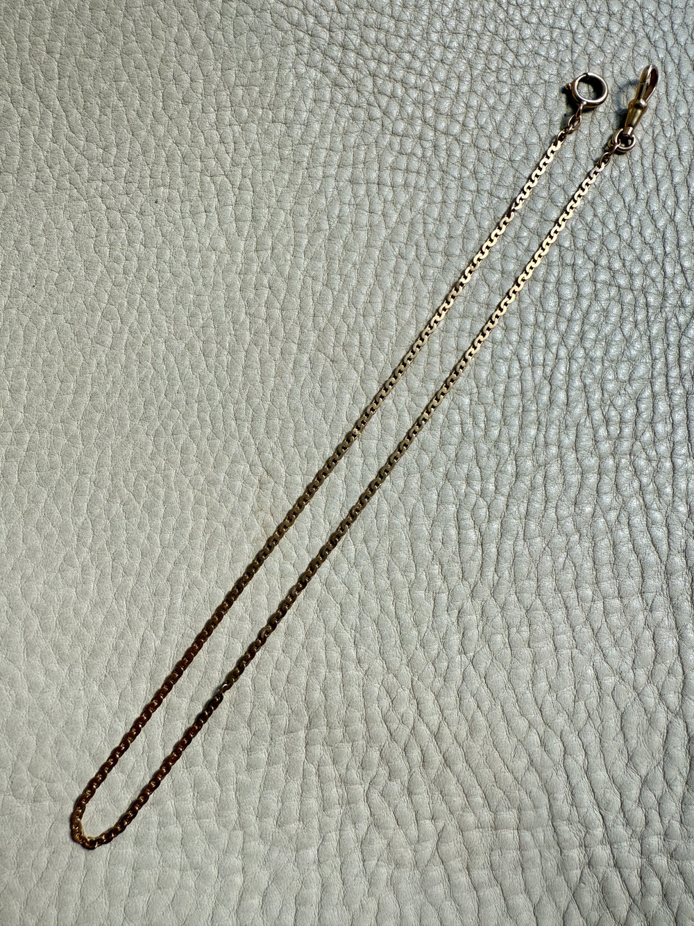 Gold 18k watch chain necklace on a textured light gray surface