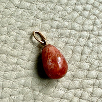 Sunstone teardrop pendant on a gold ring against a gray background