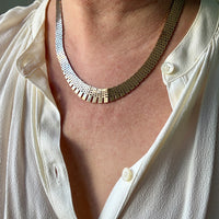 Close-up of a person wearing a gold necklace with a white shirt.