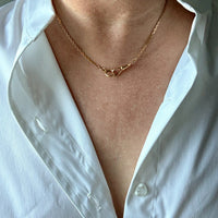 Person wearing a gold chain necklace with a white shirt.