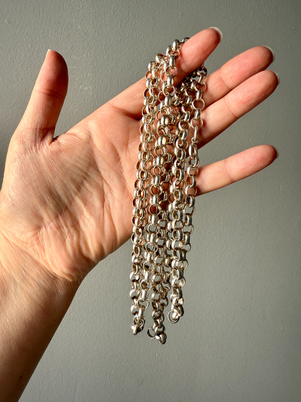 Hand holding a long silver chain against a neutral background