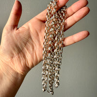 Hand holding a long silver chain against a neutral background