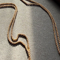 Gold rolo chain necklace on a textured gray surface