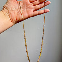 Gold chain held by a hand against a gray background