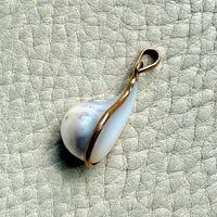 Pearl pendant with gold setting on a textured light gray background