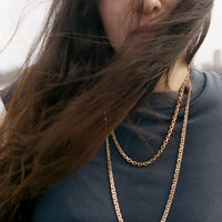 Woman with long hair and gold chain necklaces against a blurred background