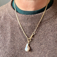 Gold necklace with a pendant worn by a person in a brown sweater.