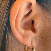 Close-up of an ear wearing a gold hoop earring with hair partially covering the frame.