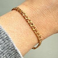 Gold chain bracelet on a wrist with a neutral background
