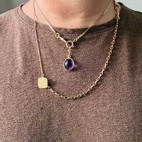 Gold necklace with a pendant worn by a person on a plain background