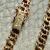 Gold chain necklace with a clasp on a textured light gray background