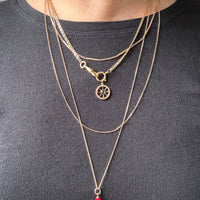 Person wearing multiple vintage 18k gold necklaces with a red pendant on a plain background penelopepenelope.com