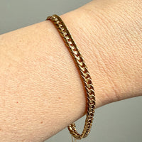 Gold chain bracelet on a wrist against a neutral background