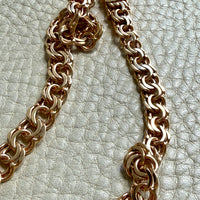 A close-up of a chunky 18k gold chain necklace laid on a textured off-white surface.