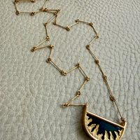 Gold necklace with a half-moon pendant on a textured beige background
