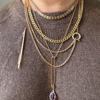 Person wearing multiple gold necklaces with a brooch on a gray background